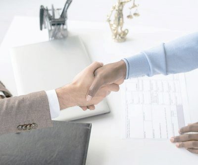 Arbeitsrecht Zwei Personen schütteln sich die Hände über einem Tisch mit Dokumenten.